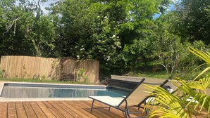 Piscina com deck de madeira, cadeiras de descanso e cerca de bambu.