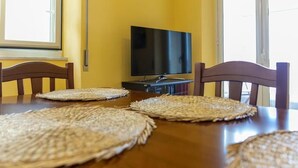 A dining table with woven placemats, a television, and wooden chairs in a room with yellow walls. - Large Apartment with Sea View and Parking in the center of Acireale. (Acireale)