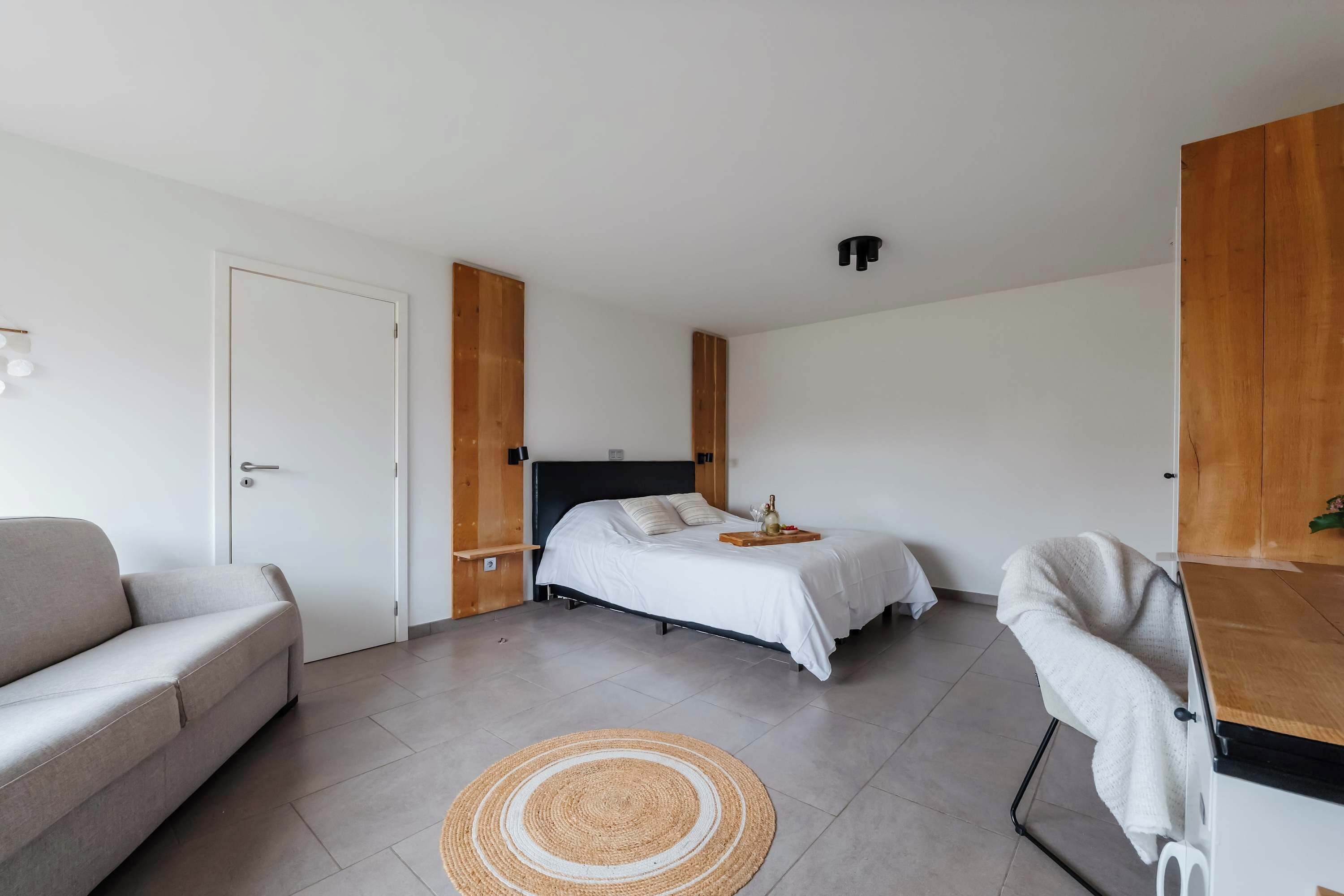 Quarto moderno com cama, sofá, poltrona e guarda-roupa de madeira.