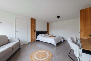 A modern bedroom with a bed, a sofa, a chair, and a wooden wardrobe. - Boutique hotel het Zoete Zijn Borgloon - Suite 2 (Tongeren-Borgloon)