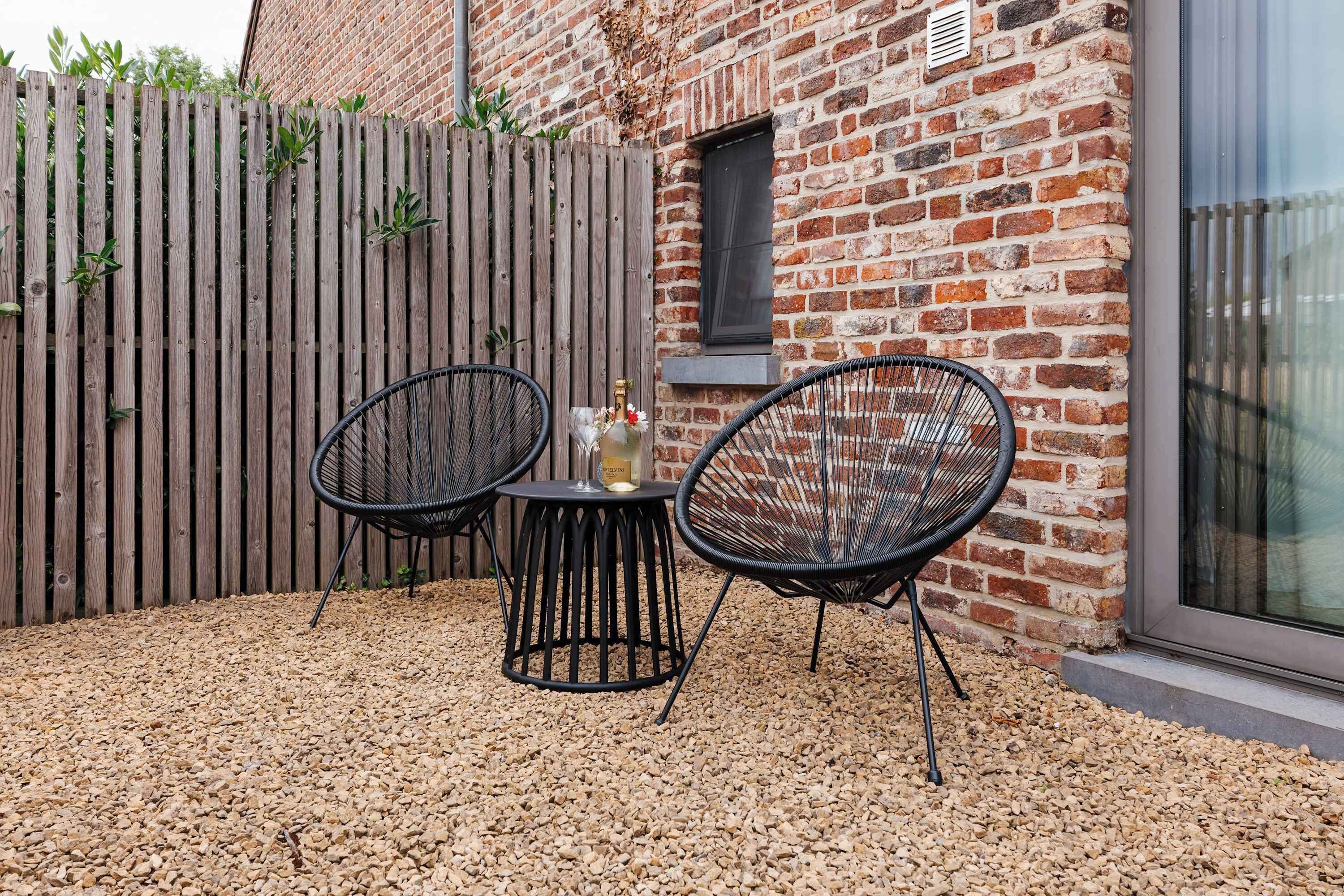 Une terrasse avec deux chaises en osier noir, une petite table ronde et une bouteille de champagne.