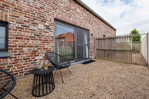 A brick building with a sliding glass door, a patio area with a table and chairs, and a wooden fence. - Boutique hotel het Zoete Zijn Borgloon - Suite 2 (Tongeren-Borgloon)