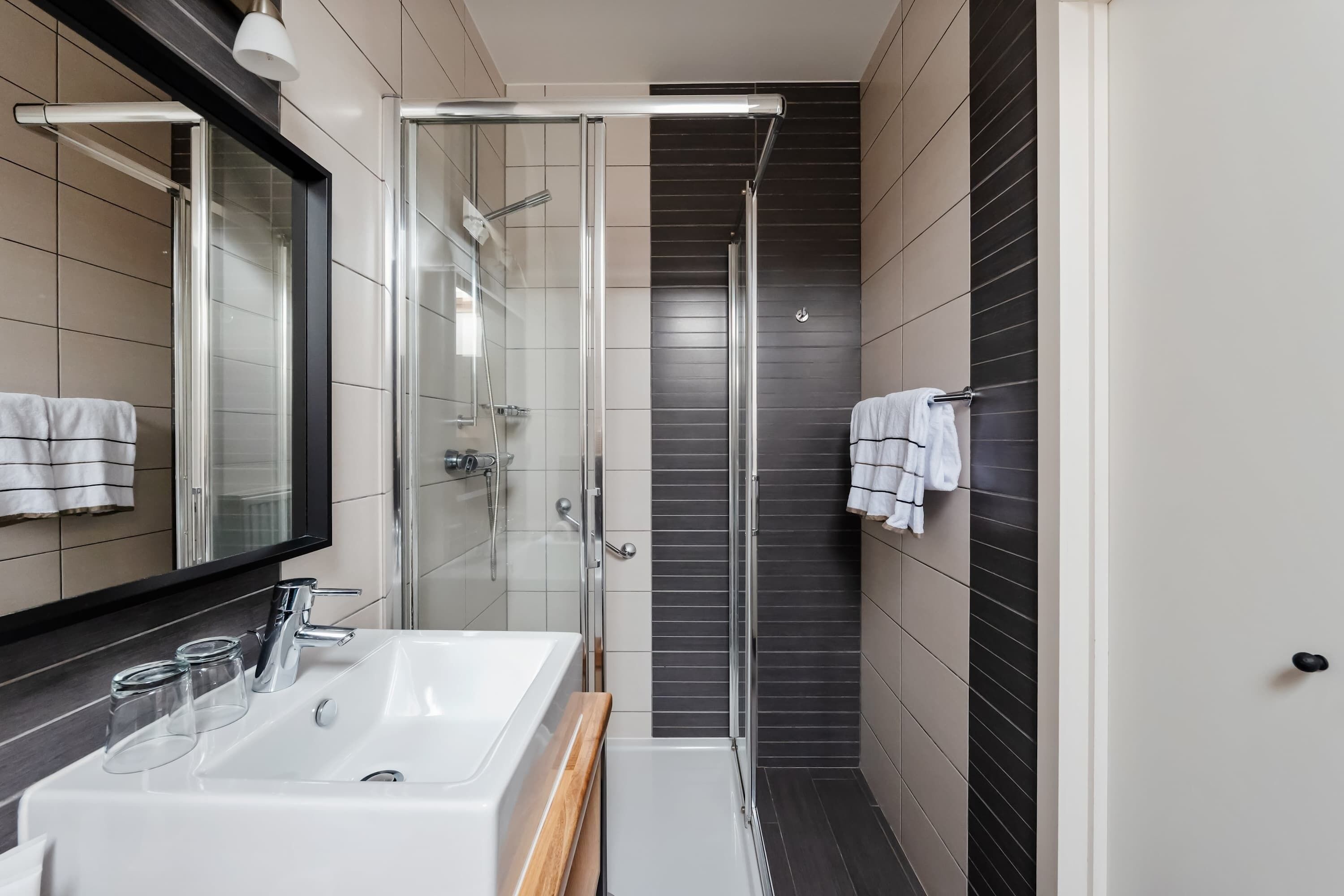 Un bany modern amb box de dutxa de vidre, un lavabo blanc i un mirall.