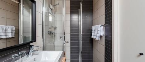 Un bany modern amb box de dutxa de vidre, un lavabo blanc i un mirall.