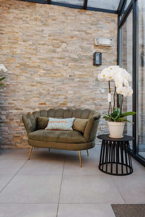 A green sofa with a patterned pillow, a potted orchid, and a small round table with a black base. - Luxe hoeve voor groepen tot 26 pers in Borgloon (Tongeren-Borgloon)