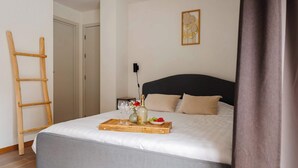 Un letto rifatto con cura, un vassoio con cibo e bevande, una scala di legno e un quadro appeso al muro.