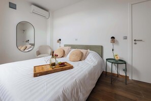 Quarto com cama, uma cadeira, mesa de cabeceira com abajur e ar-condicionado fixado na parede.