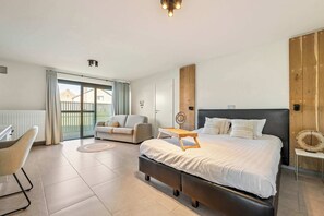 Un dormitorio con una cama grande, un escritorio, una silla, un sofá y vistas al exterior.