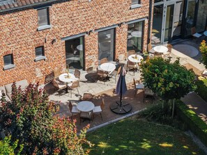 A brick building with outdoor seating and a garden area. - Luxe hoeve voor groepen tot 26 pers in Borgloon (Tongeren-Borgloon)