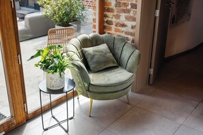A green armchair with a cushion, a small table with a potted plant, and a glass door leading outside. - Luxe hoeve voor groepen tot 26 pers in Borgloon (Tongeren-Borgloon)
