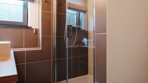 Une salle de bain avec une douche à parois de verre, une fenêtre et des toilettes.