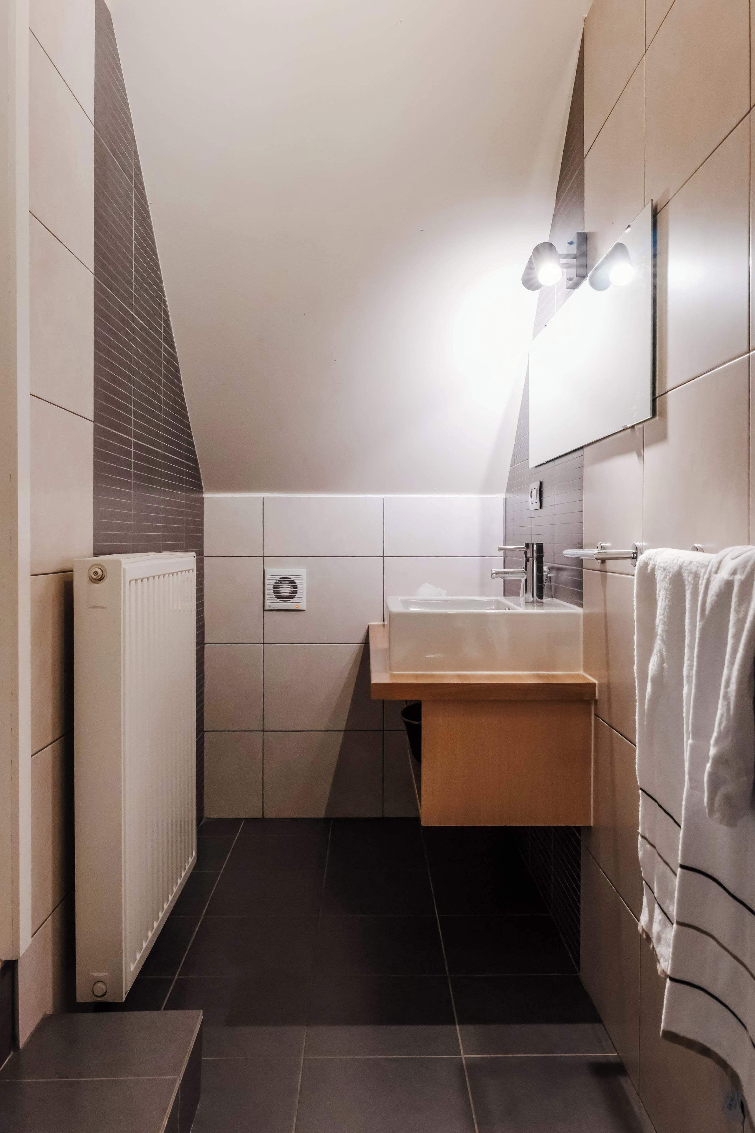 A modern bathroom with a sloped ceiling, a radiator, a sink, and a towel rack.