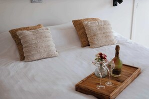 A neatly made bed with white linens and two textured pillows, a wooden tray with a bottle and glasses, and a small vase with flowers. - Boutique hotel het Zoete Zijn Borgloon - Suite 4 (Tongeren-Borgloon)