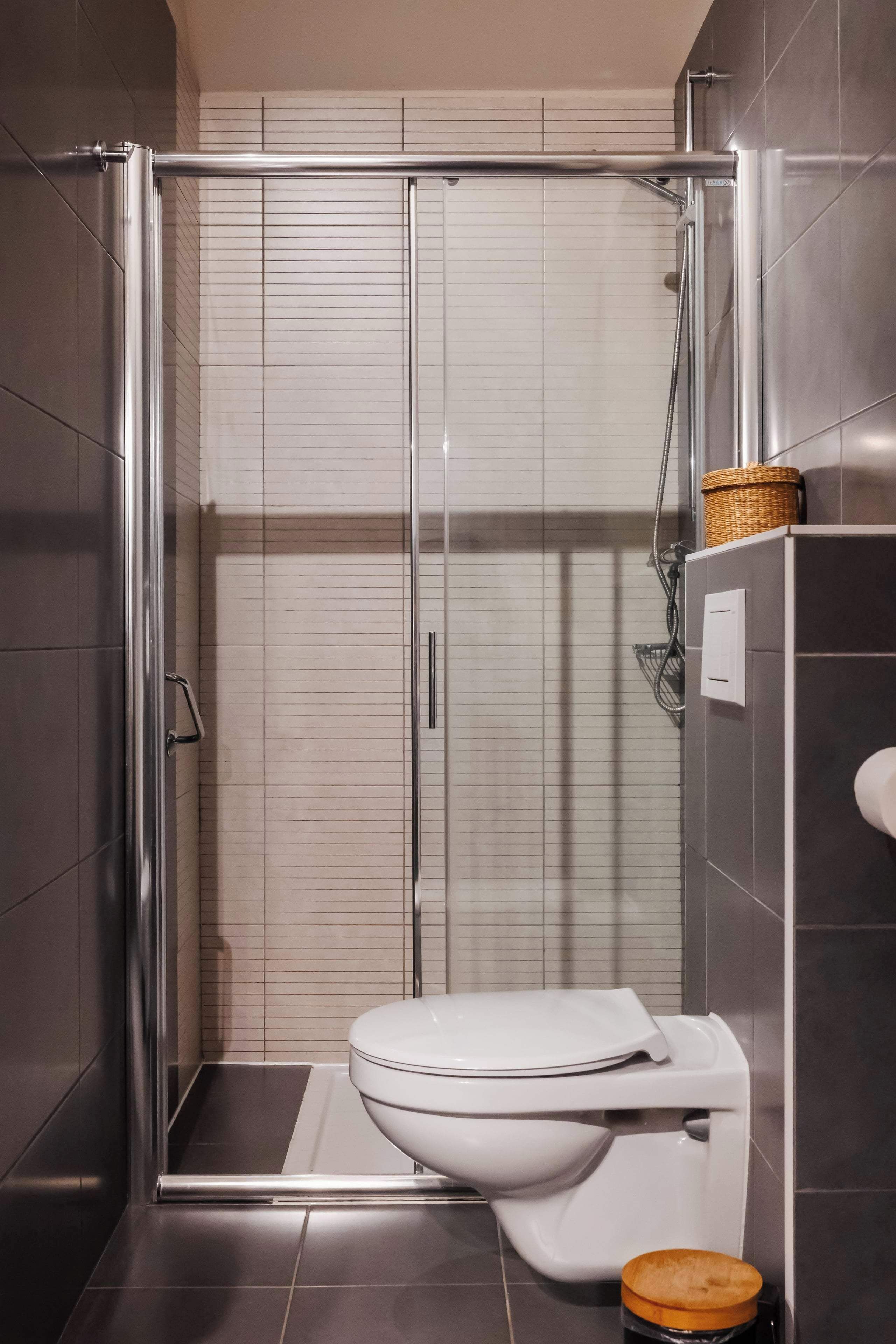 Een moderne badkamer met een douchecabine van glas, een wit toilet en een klein houten krukje.