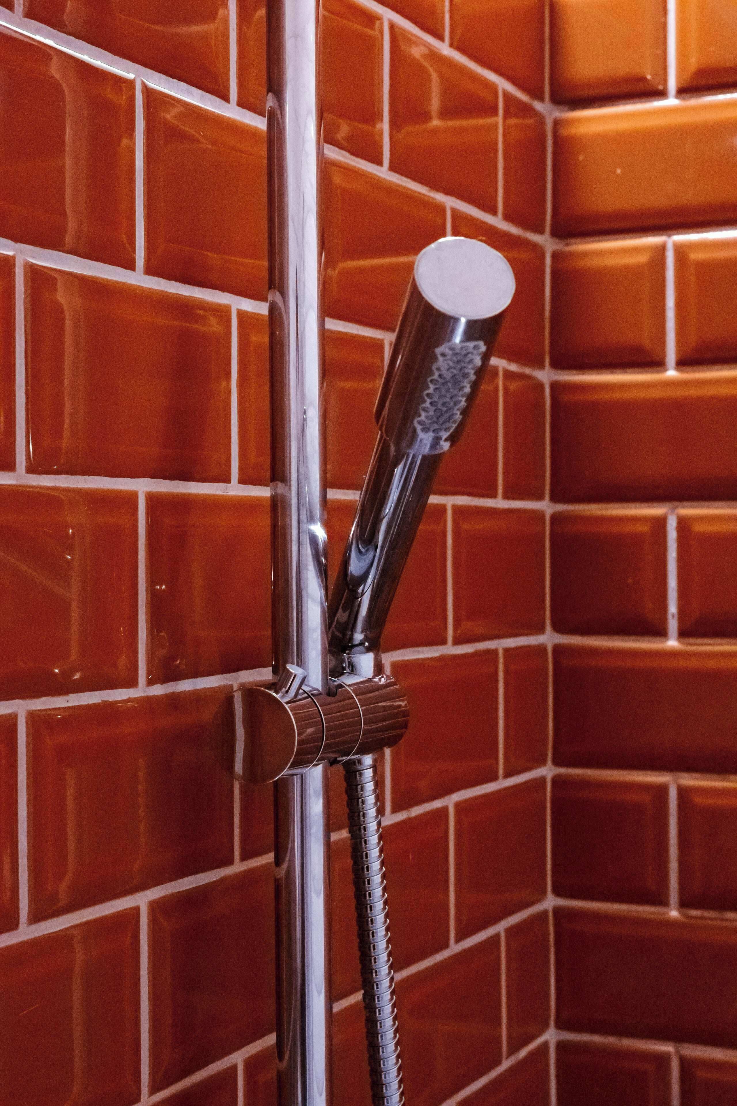 Een douchekop bevestigd aan een metalen pijp met een gestructureerd handvat, tegen een betegelde muur.