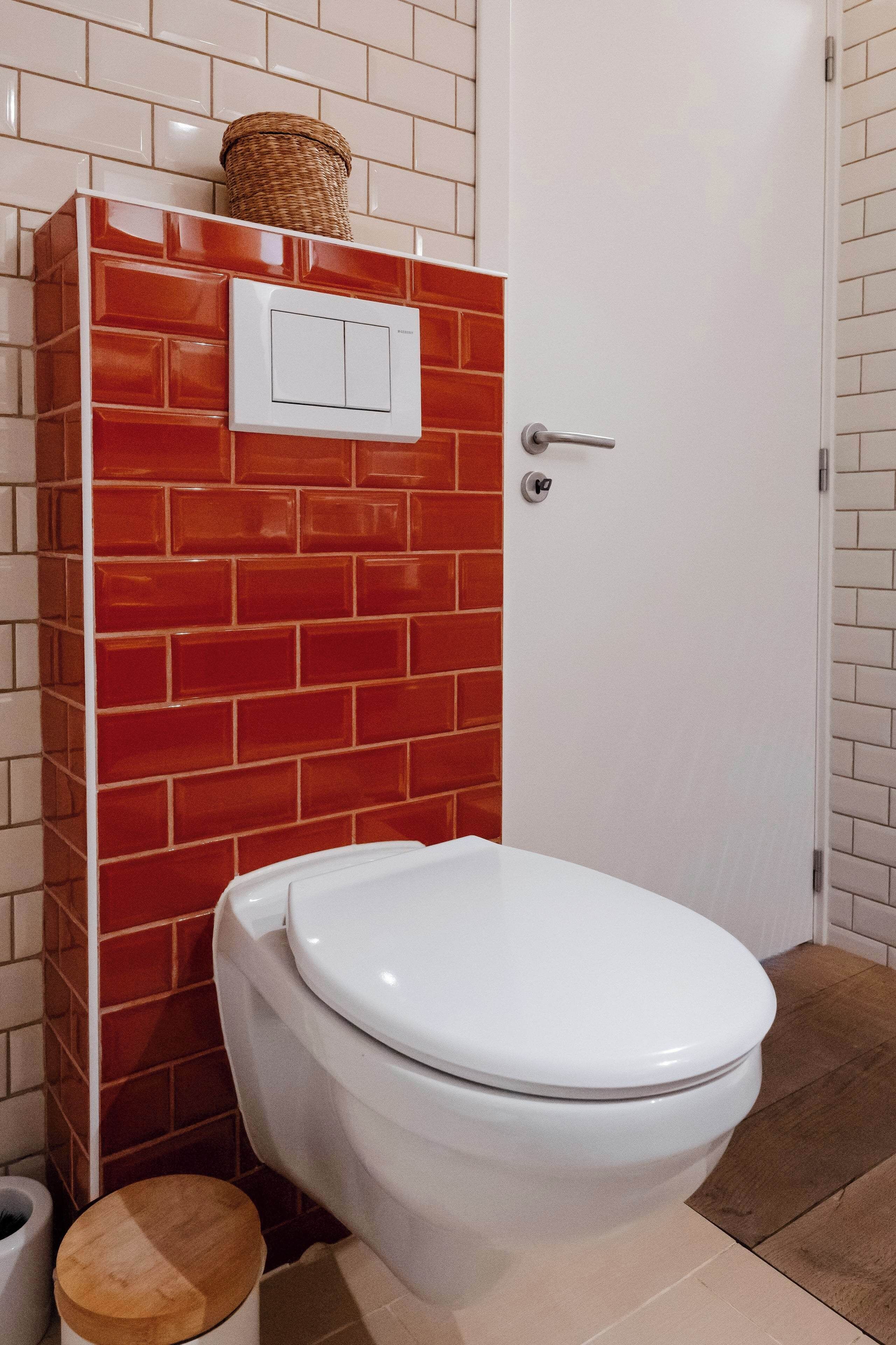 Une salle de bain avec des toilettes blanches, un mur en briques rouges et une porte blanche.