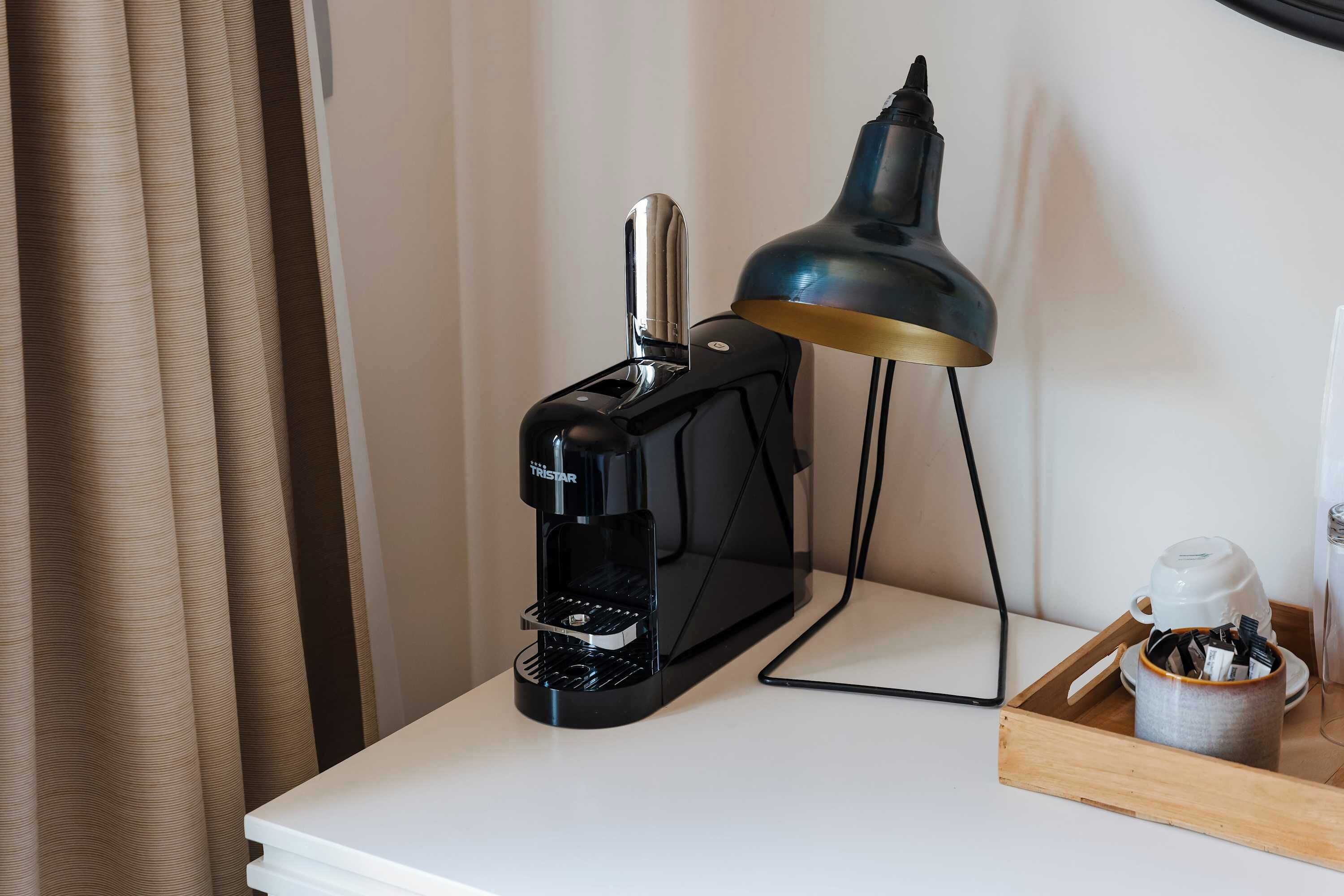 A coffee maker, a lamp, and a tray with a cup and utensils on a white table.