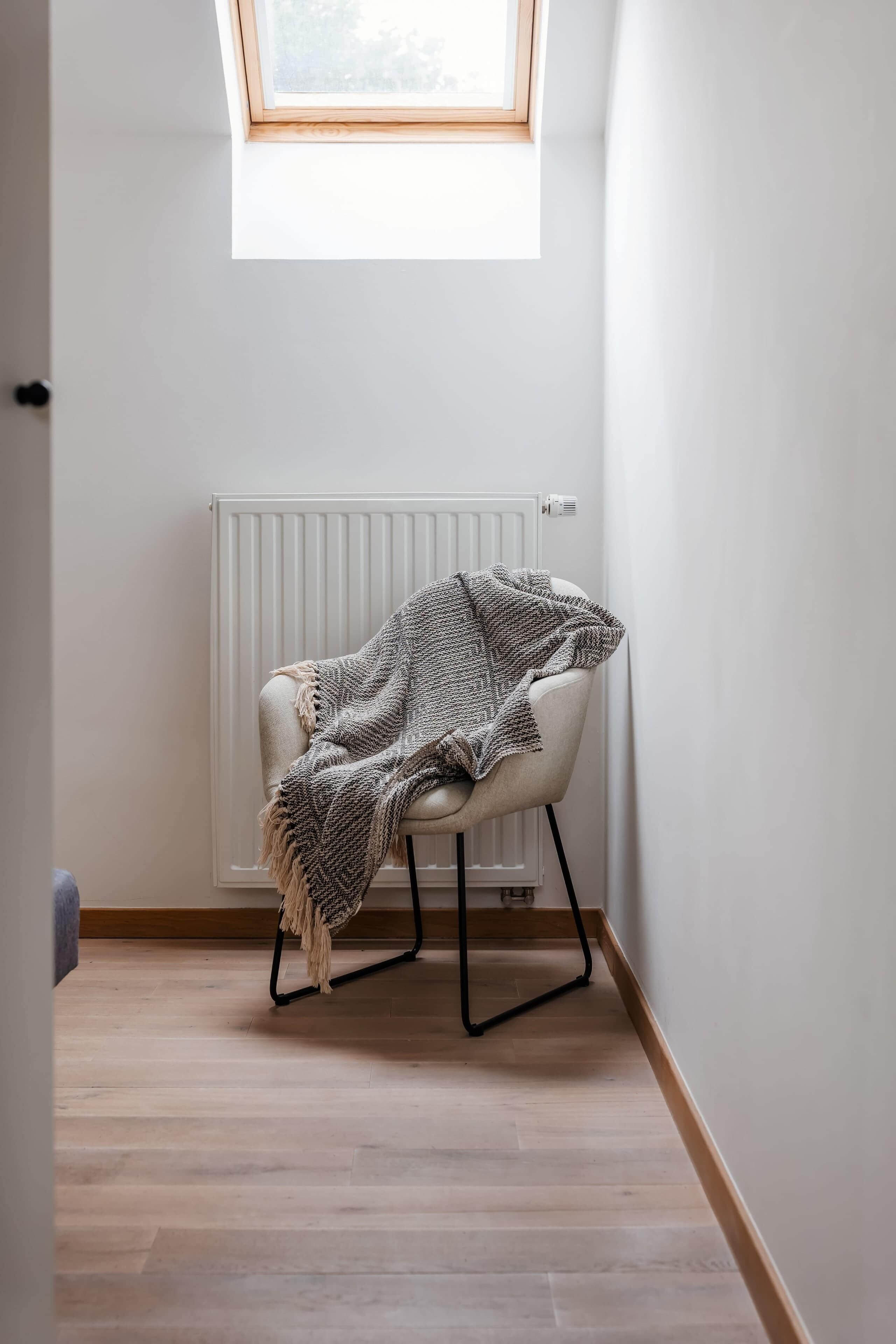 Ein Zimmer mit einem weißen Heizkörper, einem Sessel mit gemustertem Überwurf und einem Oberlicht.