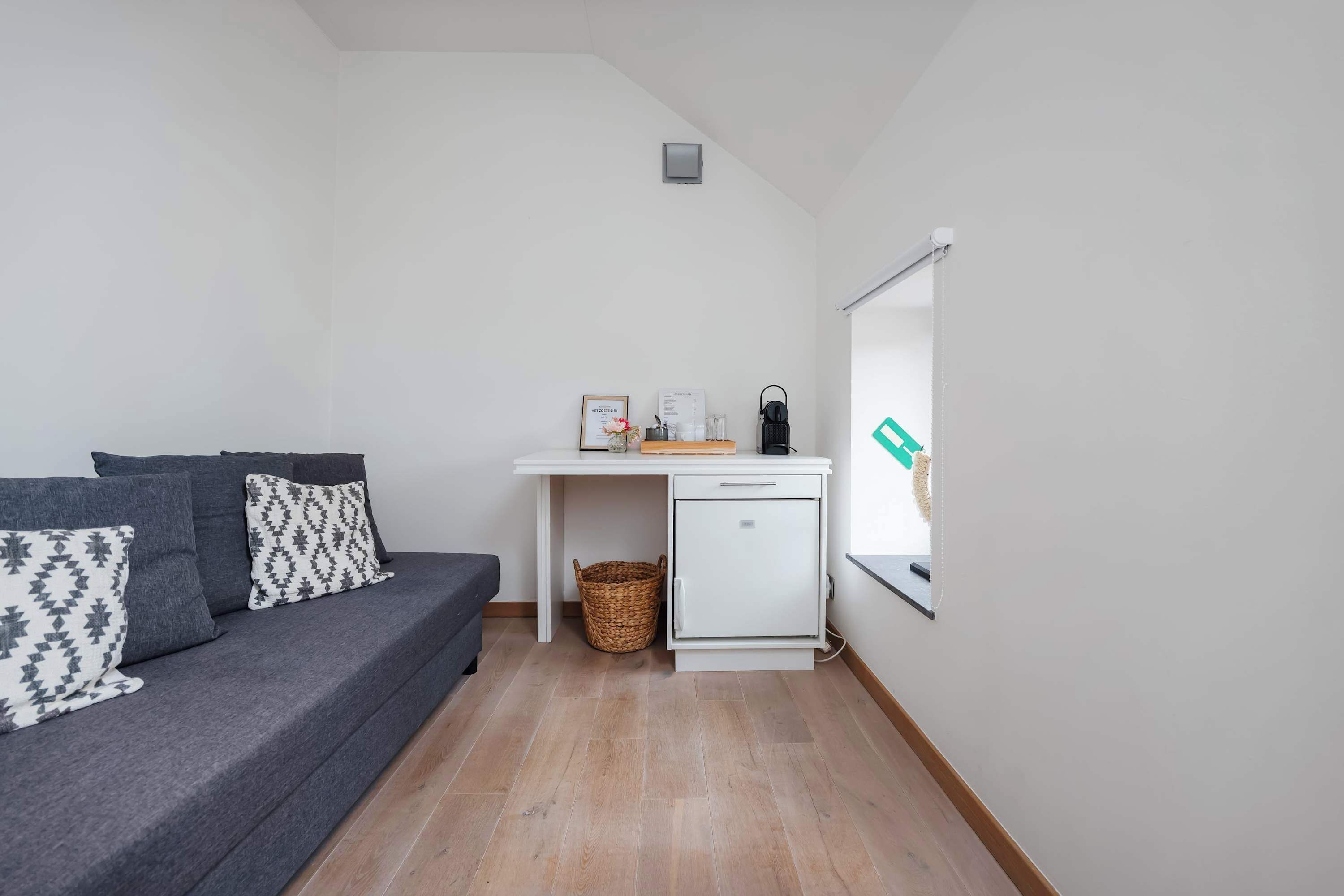 A compact living space with a sofa, a small desk, a basket, and a window.