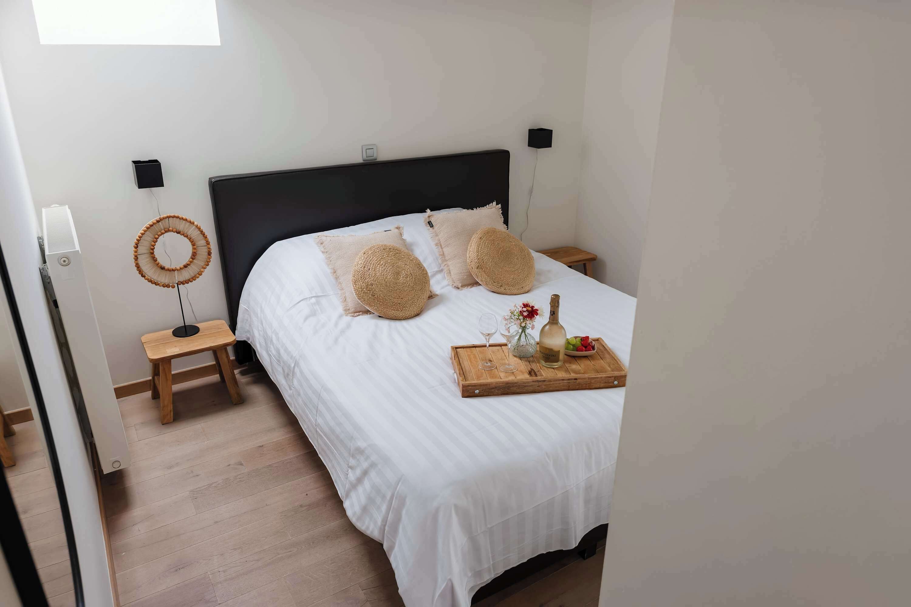 A bedroom with a bed, bedside tables, a wall-mounted speaker, and a small stool.