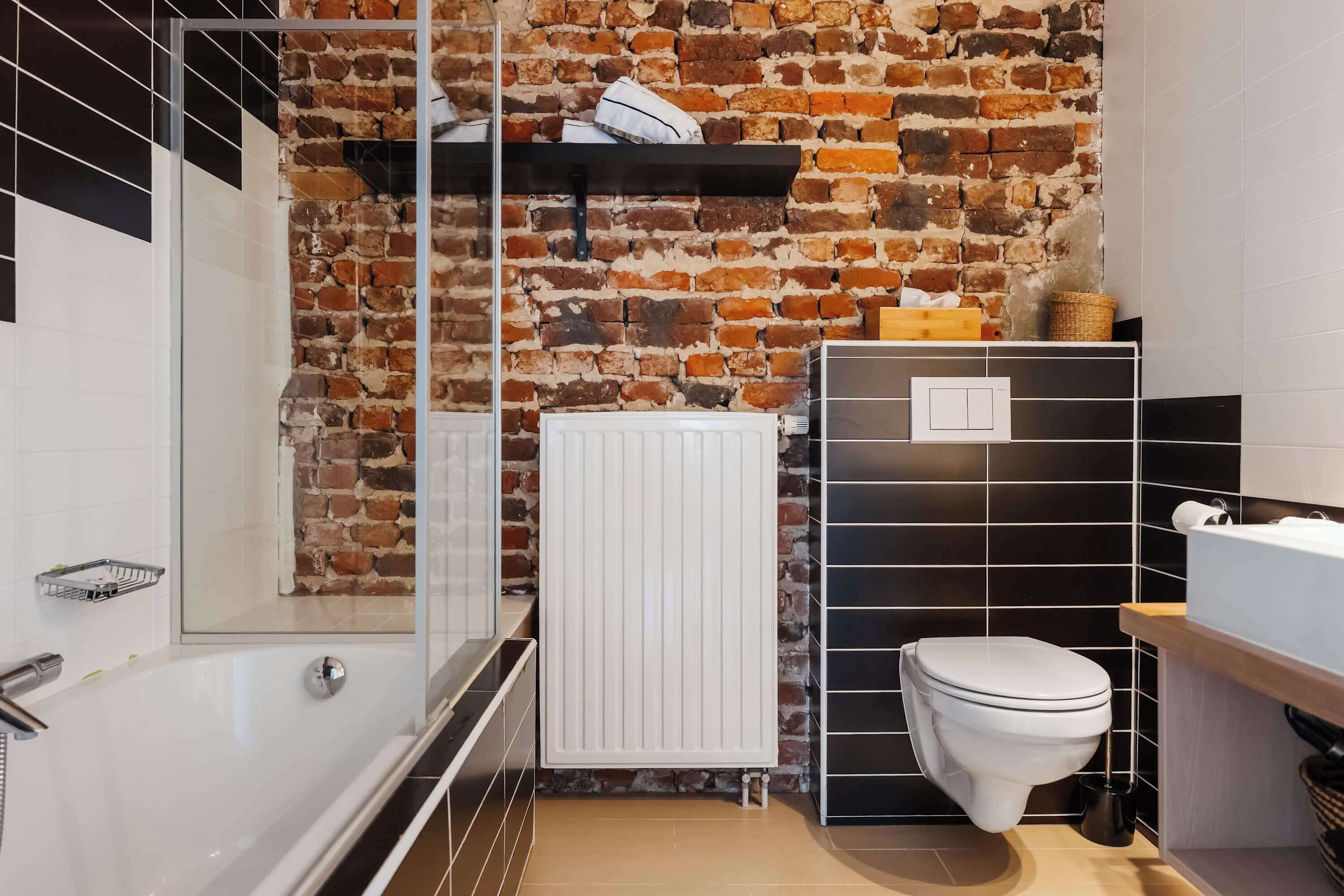 Een badkamer met een bakstenen muur, een witte radiator, een toilet en een douchecabine van glas.