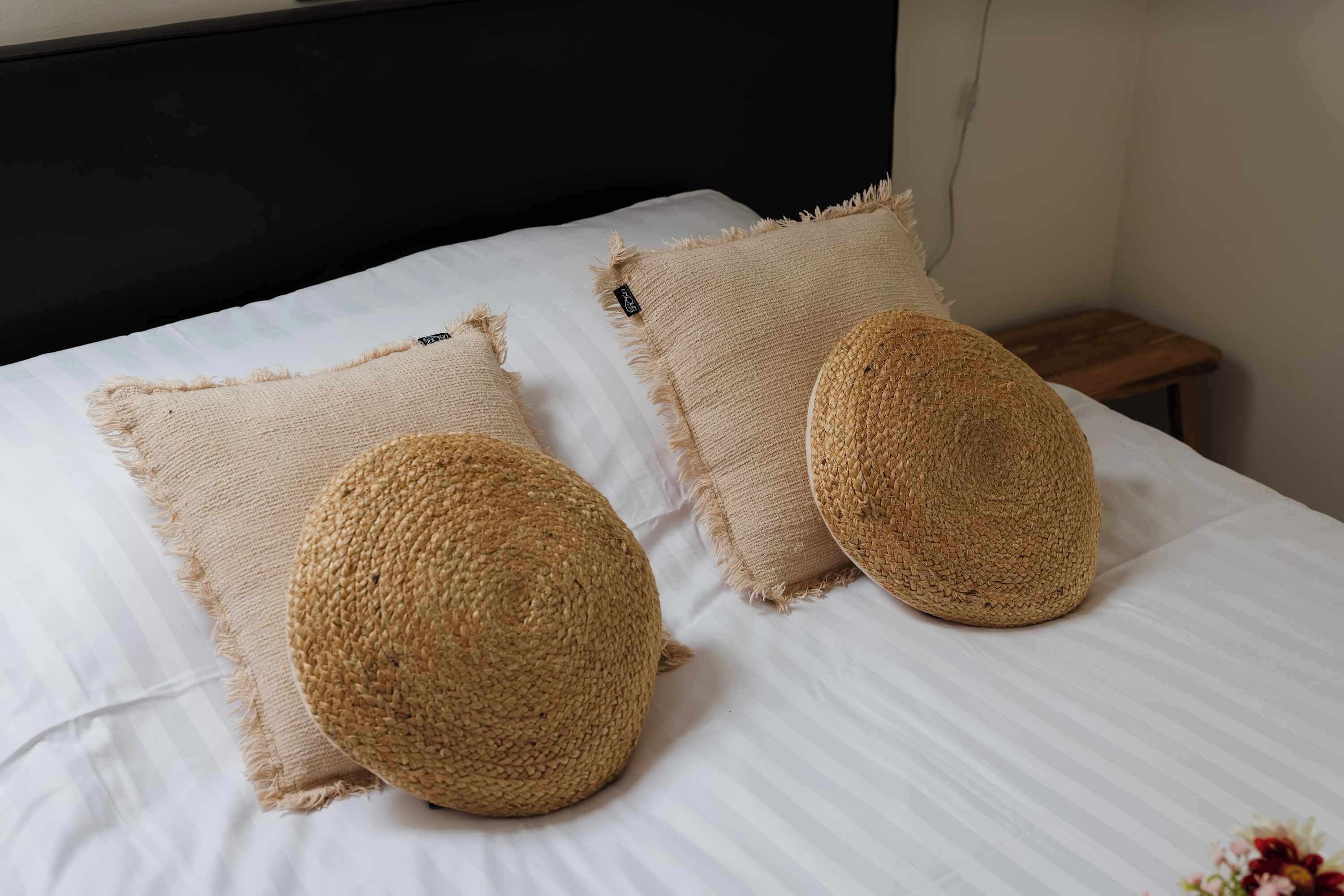 A bed with two square and two round woven pillows.