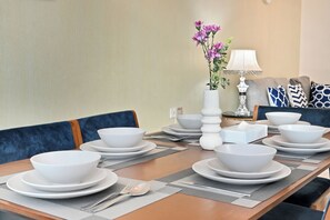 Ein Esstisch, gedeckt mit weißen Schalen und Tellern, eine Vase mit Blumen und eine Lampe.
