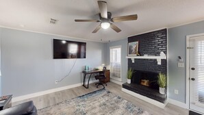 Ein Wohnzimmer mit Kamin, Deckenventilator, Wand-Fernseher und Schreibtisch mit Stuhl.
