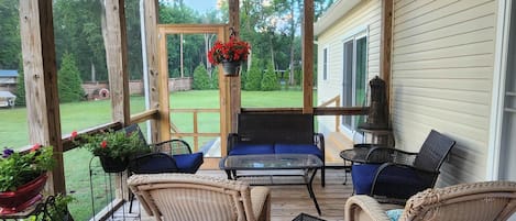 A covered porch with wicker furniture, a table, and potted plants.