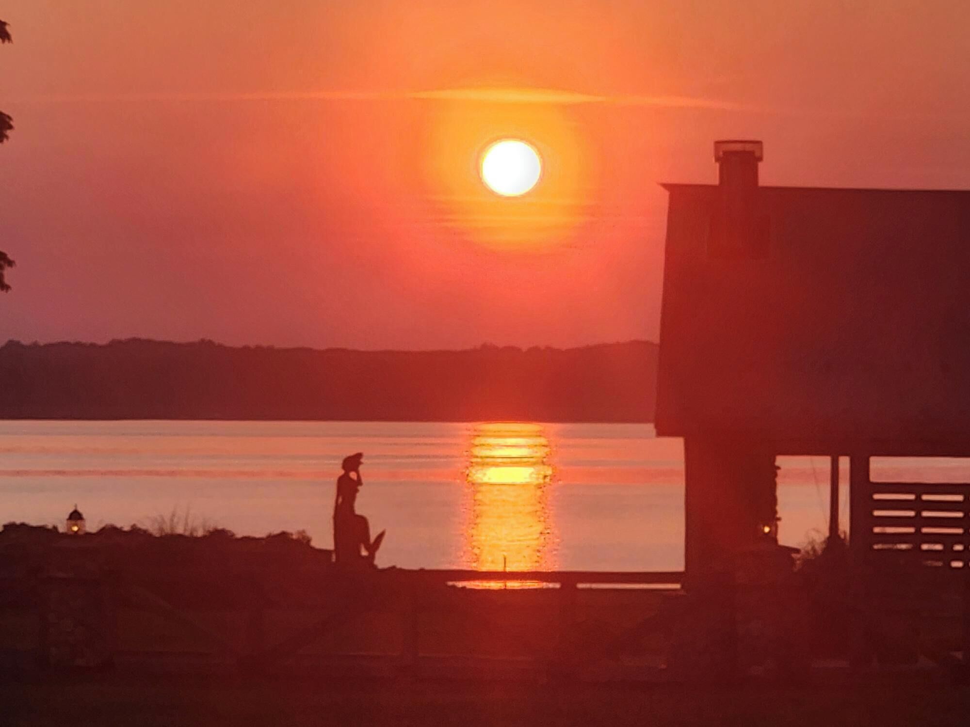 Un atardecer sobre un cuerpo de agua, con la silueta de una persona y un edificio al frente.