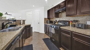 Una cocina moderna con armarios de madera oscura, encimeras de granito, electrodomésticos de acero inoxidable y un tapete negro en el suelo.