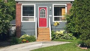 Ein zweistöckiges Haus mit roter Haustür, einer kleinen Veranda und einem Ziegelkamin.