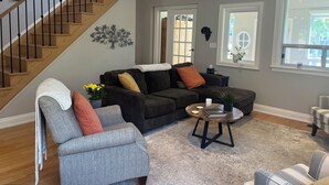 Ein Wohnzimmer mit Treppe, grauem Sofa, Couchtisch und Topfpflanze.