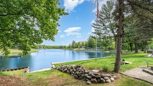 A serene lakeside setting with a dock, a pile of rocks, and a flagpole. - Stunning Lakefront Cottage with Beach & Hot Tub (Alger)