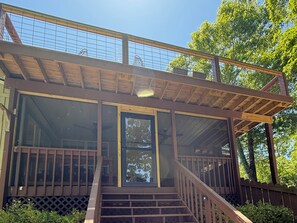 A wooden cabin with a covered porch, a staircase, and a large window.