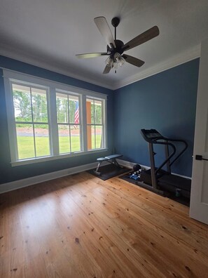 Ein Zimmer mit Deckenventilator, großen Fenstern, Laufband und Holzboden.