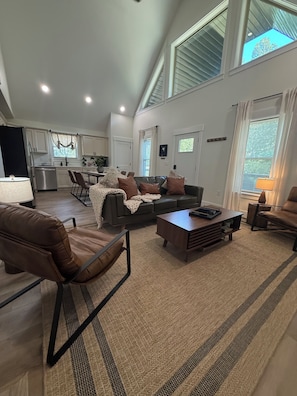 A spacious living area with a high ceiling, a dining table, and a kitchen in the background.