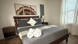 Ein Schlafzimmer mit einem Bett, einem Nachttisch, einem Deckenventilator und einem Fenster mit Vorhängen.