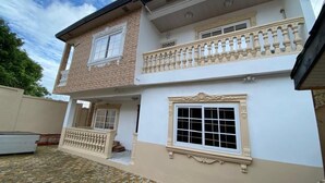 En toetages bygning med en balkon på øverste etage, et stort vindue på nederste etage og en gårdhave med stenbelægning.