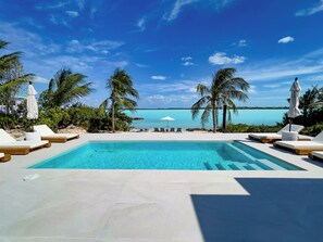 Ein Pool mit Liegestühlen und Sonnenschirmen, umgeben von Palmen und Blick auf den Ozean.