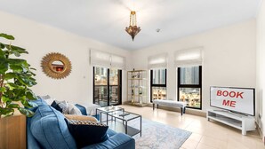A modern living room with a blue sofa, a glass coffee table, and a TV on a stand. - Stayshort - 2 Bedroom in Oldtown Sleeps 4 Close to Burj Khalifa (Dubai)