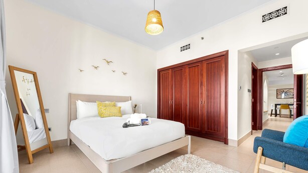 A bedroom with a bed, a wooden wardrobe, a mirror, and a hanging light fixture. - Stayshort - 2 Bedroom in Oldtown Sleeps 4 Close to Burj Khalifa (Dubai)