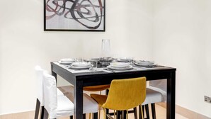 A dining table set with plates, glasses, and cutlery, a vase, and a framed abstract painting on the wall. - Stayshort - 2 Bedroom in Oldtown Sleeps 4 Close to Burj Khalifa (Dubai)