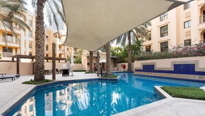 A swimming pool with a tiled edge, surrounded by palm trees and a covered seating area. - Stayshort - 2 Bedroom in Oldtown Sleeps 4 Close to Burj Khalifa (Dubai)