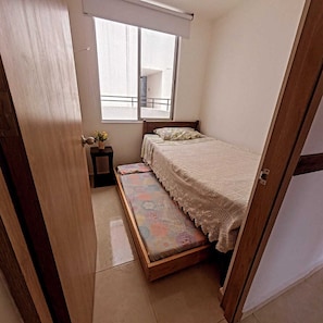 A small bedroom with a bed, a bench, a nightstand, and a window.