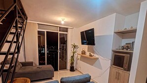 Un salon moderne avec un canapé, un téléviseur fixé au mur, un escalier et une vue sur la ville à travers les portes vitrées.