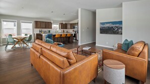 A modern living room with a leather sofa, a coffee table, and a dining area with chairs and a table. - Panoramic Views | 13 Min to Winter Park | Sleeps 8 (Tabernash)
