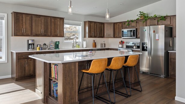 A modern kitchen with wooden cabinets, a large island with bar stools, stainless steel appliances, and pendant lighting. - Panoramic Views | 13 Min to Winter Park | Sleeps 8 (Tabernash)