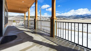 A covered outdoor area with a wooden deck, metal railing, and a view of snow-covered mountains. - Panoramic Views | 13 Min to Winter Park | Sleeps 8 (Tabernash)
