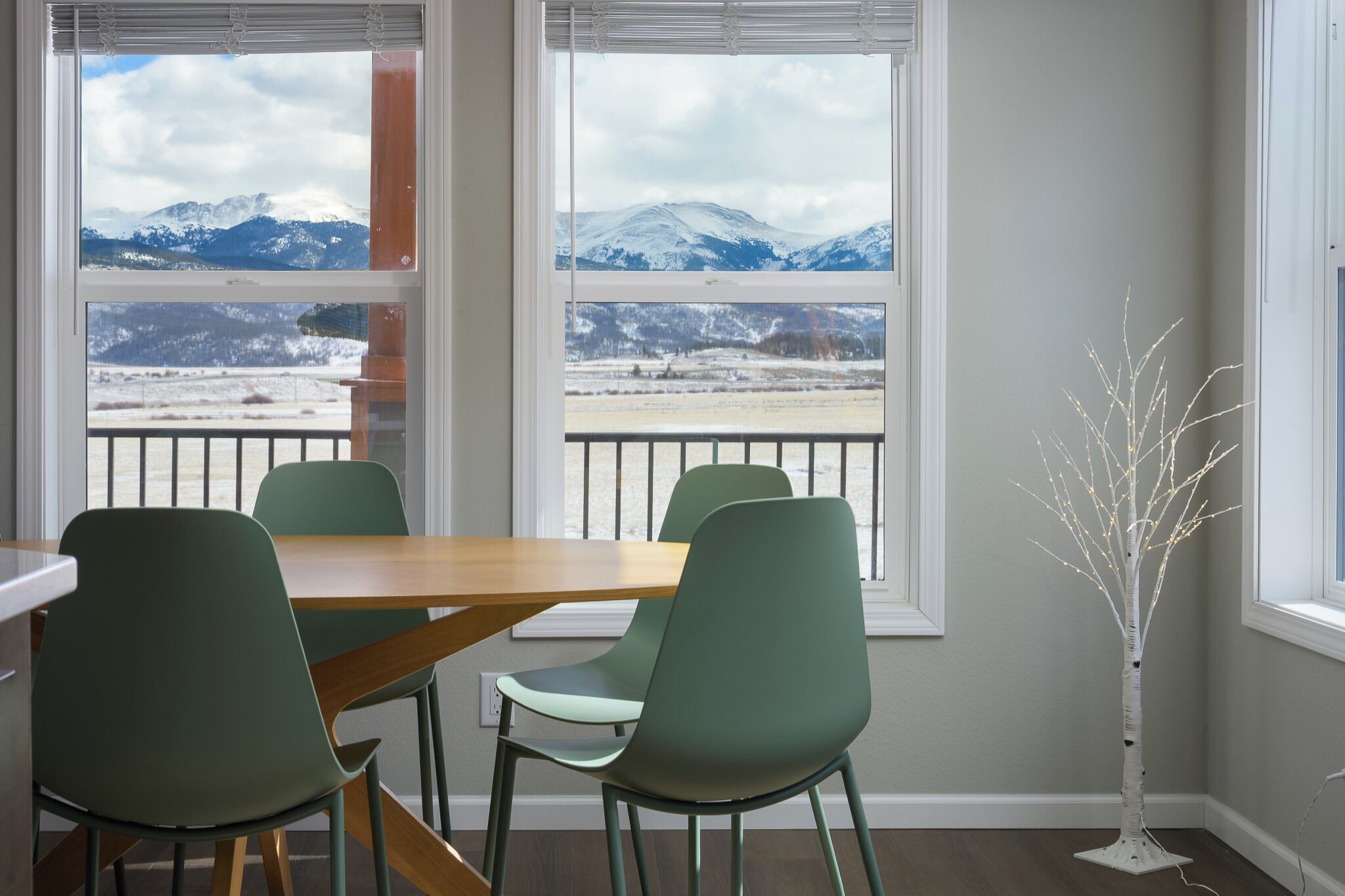 Ein Essbereich mit Tisch und Stühlen, große Fenster mit Blick auf die Berge und eine weiße Holzskulptur.